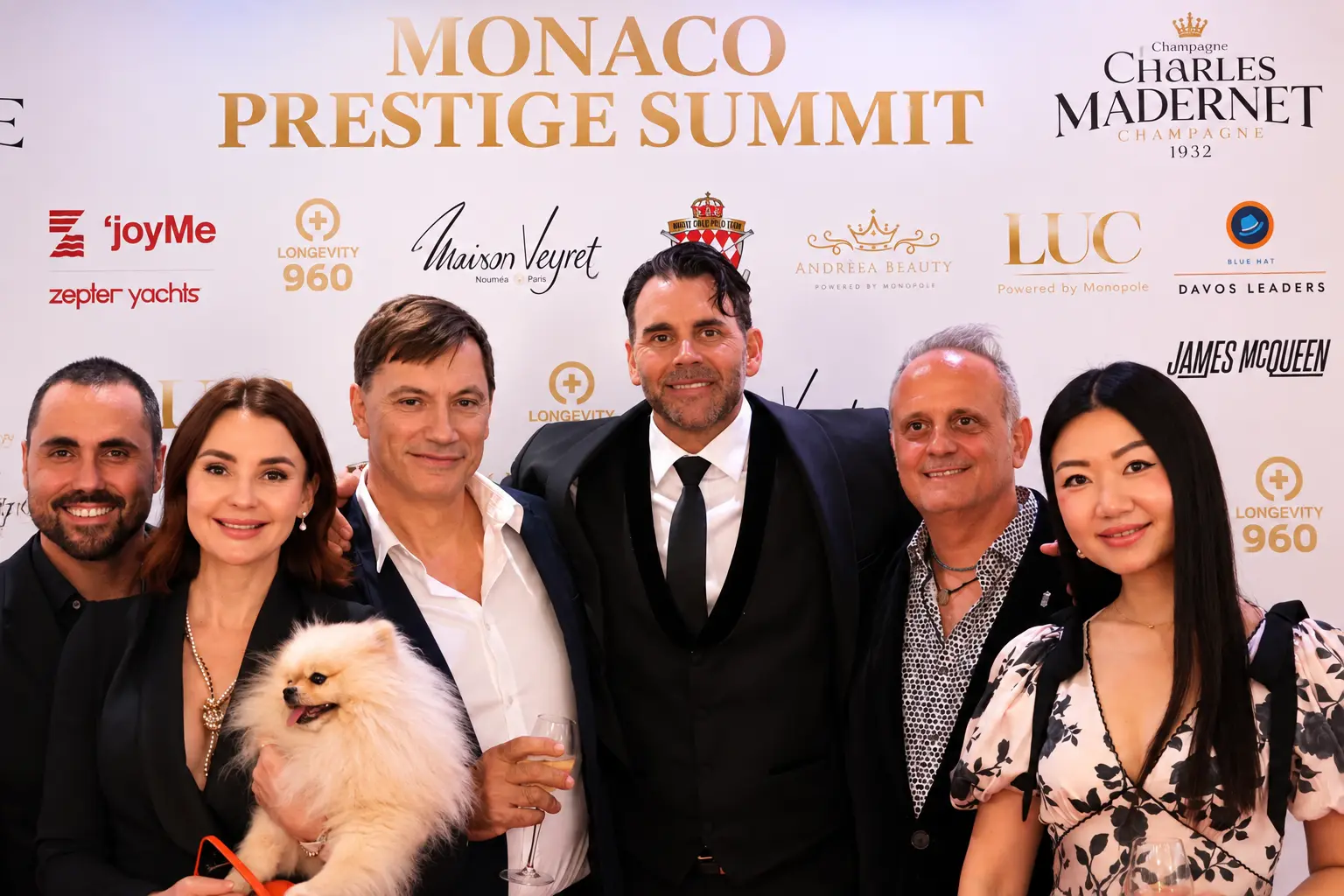 Group of six guests with a Pomeranian at the Monaco Prestige Summit media wall