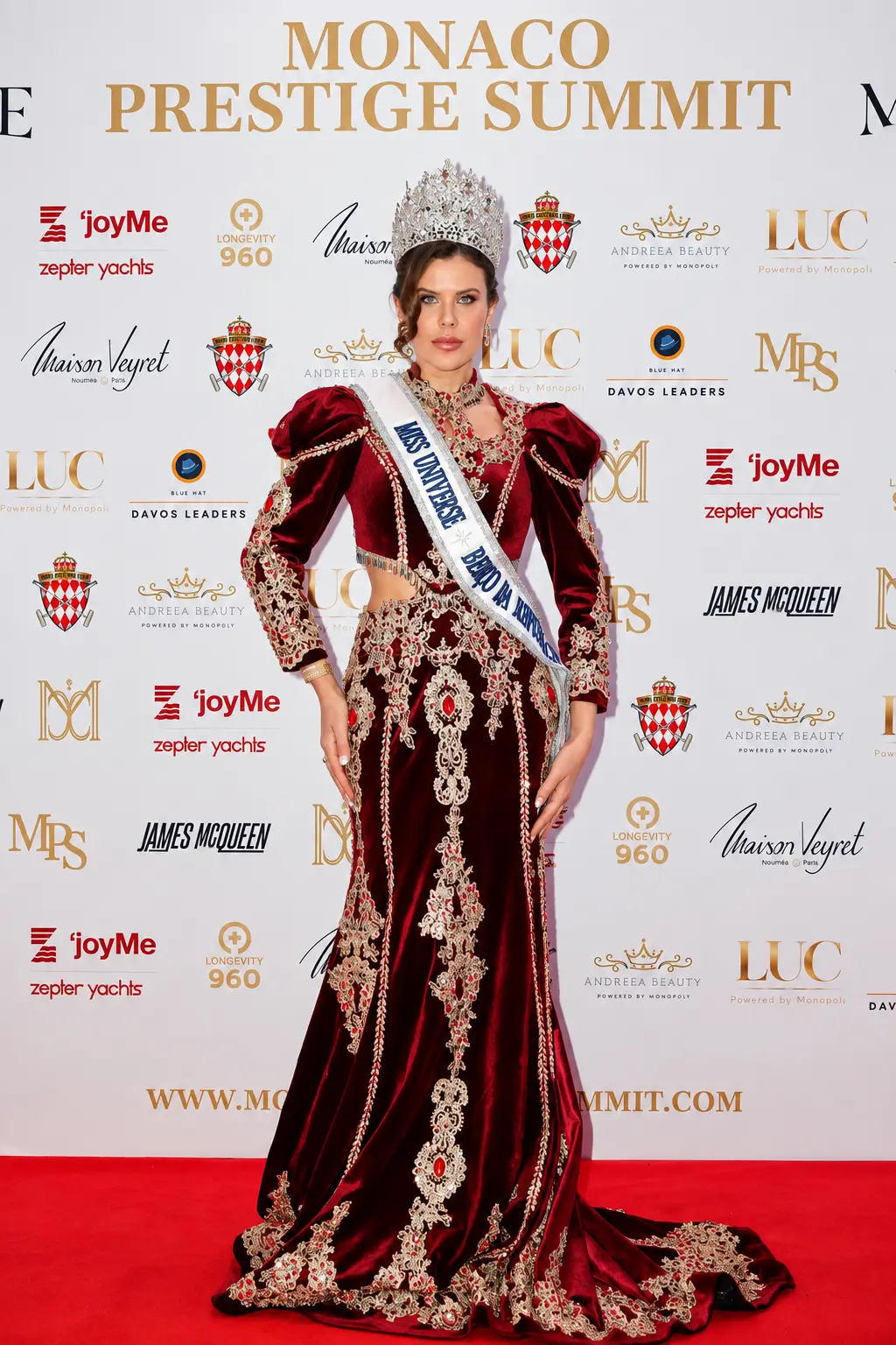 Miss Universe Puerto Rico in a burgundy gown on the red carpet at the Monaco Prestige Summit