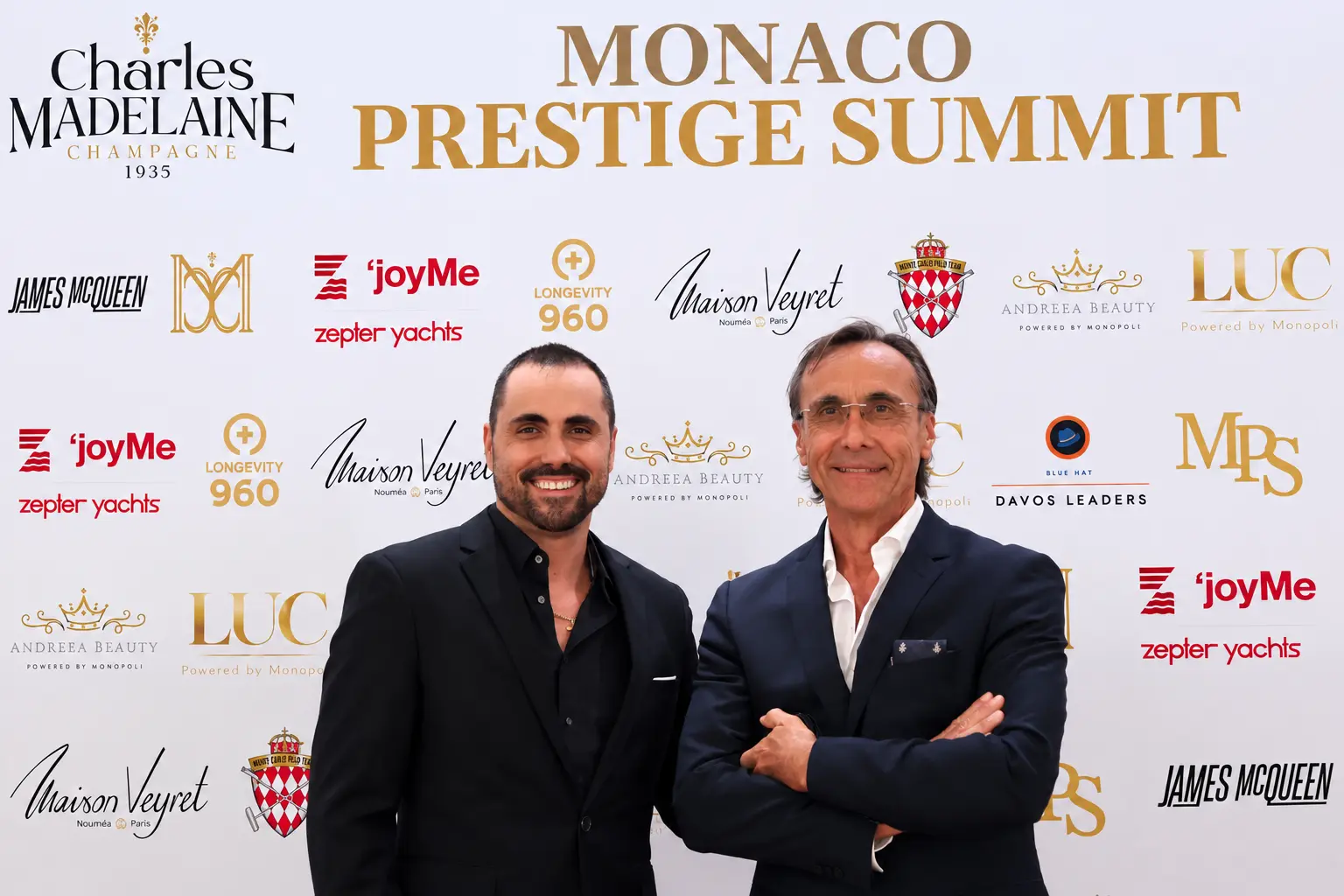Two guests in suits at the Monaco Prestige Summit media wall