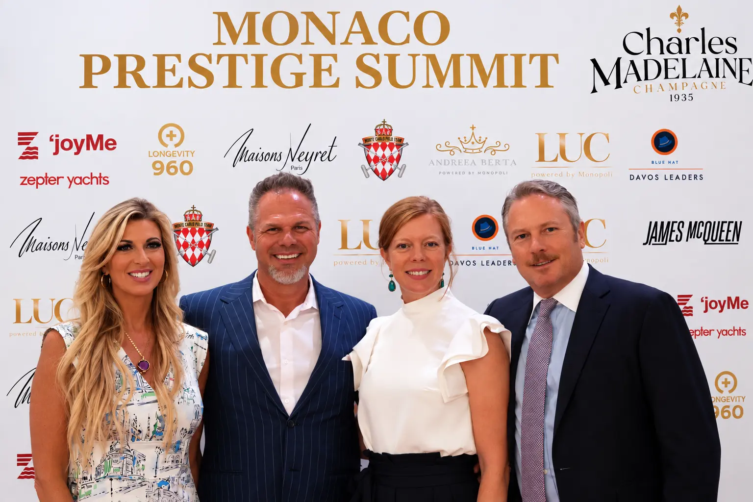 Four guests posing in front of the Monaco Prestige Summit media wall